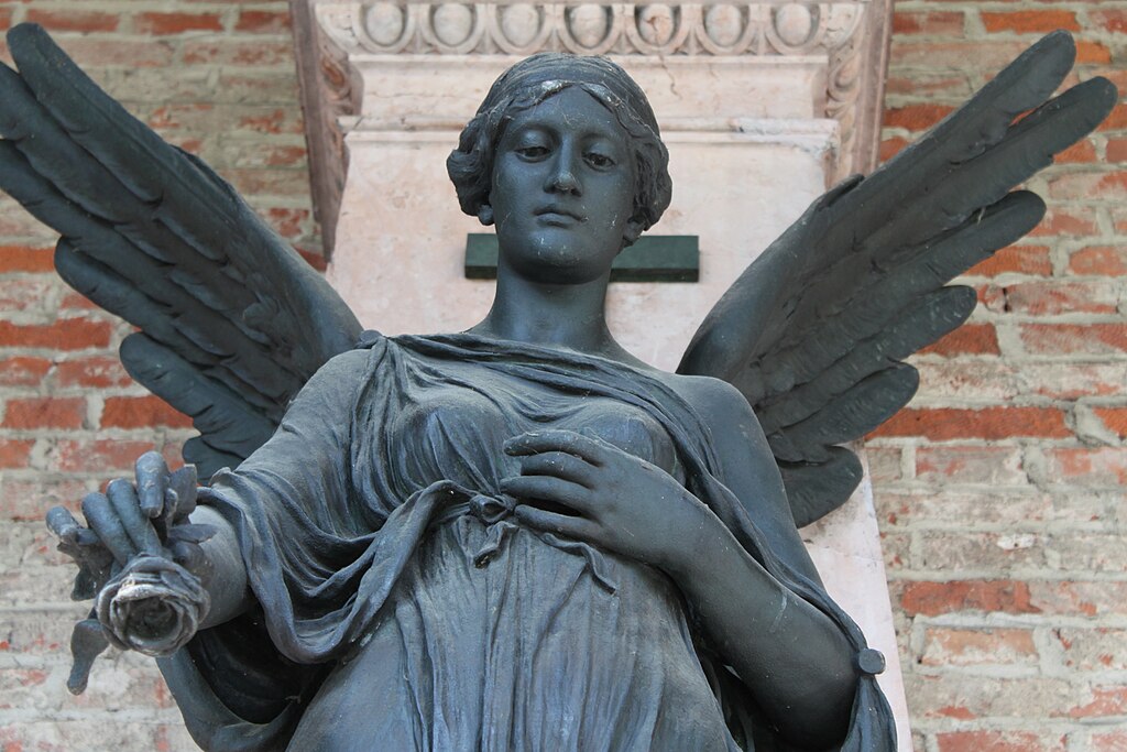 Bronzestatue einer geflügelten weiblichen Engelsfigur im Alten Südfriedhof in München, mit einem gefalteten Gewand und einer Hand, die ein Objekt hält.