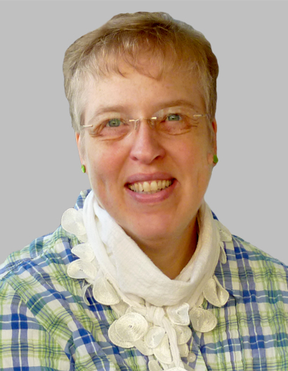 Das Porträt zeigt eine Frau in einem bunt karierten Hemd und einem weißen, dekorativen Schal vor einem neutralen grauen Hintergrund. Die Aufnahme strahlt eine freundliche und einladende Atmosphäre aus, passend zu einem Workshop-Thema rund um Ernährung und Bewusstsein.