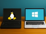 Zwei Laptops stehen auf einem hölzernen Schreibtisch. Ein Laptop zeigt das Logo von Linux, einen sitzenden Pinguin, der andere das Logo von Windows, ein stilisiertes Fenster.