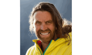 Portrait von Thomas Huber, dem erfahrenen Extrembergsteiger der ‚Huberbuam‘, in gelber Outdoor-Jacke vor alpiner Kulisse