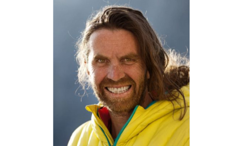 Portrait von Thomas Huber, dem erfahrenen Extrembergsteiger der ‚Huberbuam‘, in gelber Outdoor-Jacke vor alpiner Kulisse