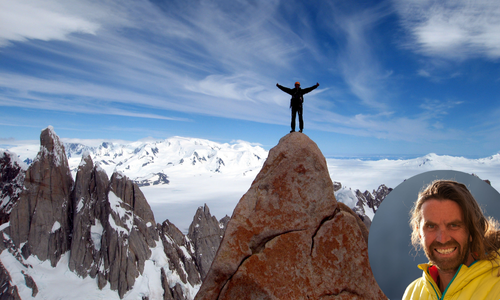 Thomas Huber steht mit ausgebreiteten Armen auf einem Berggipfel umgeben von schneebedeckten Felsen