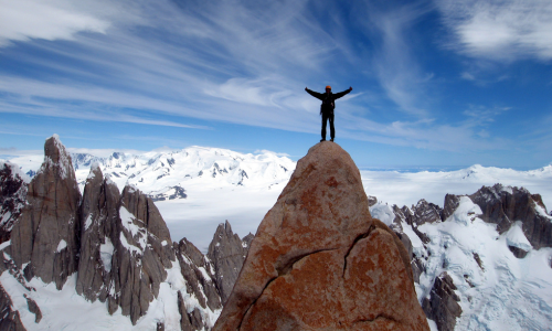 Thomas Huber steht mit ausgebreiteten Armen auf einem Berggipfel umgeben von schneebedeckten Felsen
