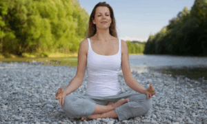 Frau sitzt in Meditationshaltung am Flussufer – Symbol für Ruhe, Atem und Achtsamkeit im Yin Yoga Herbst-Workshop der vhs Oberhaching.