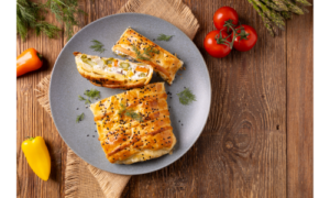 Anschnitt eines herzhaften Gemüsestrudels auf einem Teller, garniert mit frischen Kräutern