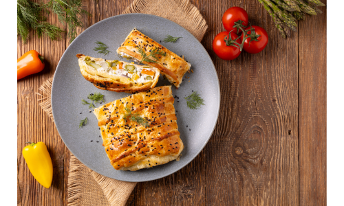 Anschnitt eines herzhaften Gemüsestrudels auf einem Teller, garniert mit frischen Kräutern