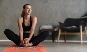 Frau sitzt entspannt auf einer Yogamatte und führt eine Dehnübung im Sitzen aus.