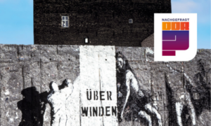 Graffiti an einer Betonmauer mit dem Schriftzug „Überwinden“ und silhouettenartigen Figuren neben einem Gebäude.
