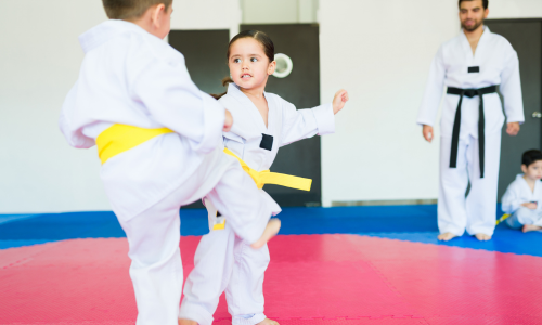 Zwei Kinder üben Taekwon-Do-Techniken, während ein Trainer das Training begleitet.